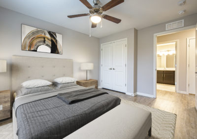 Model apartment bedroom with large bed, walk-in closets, and master bathroom at Goodnight Commons