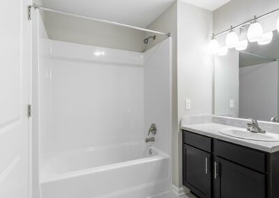 Model bathroom with large vanity, mirror, and shower in an apartment at Goodnight Commons