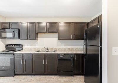 Model kitchen with chocolate cabinetry and black appliances in Goodnight Commons apartment